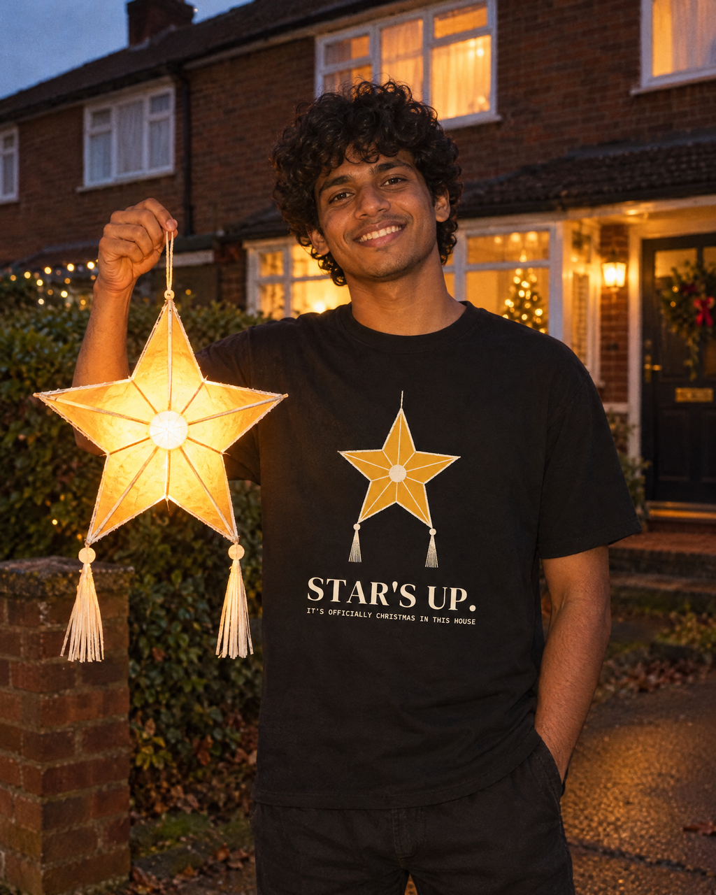 Lifestyle image (AI-generated illustration): man wearing the Star's Up Tee in Black, holding a paper star lantern